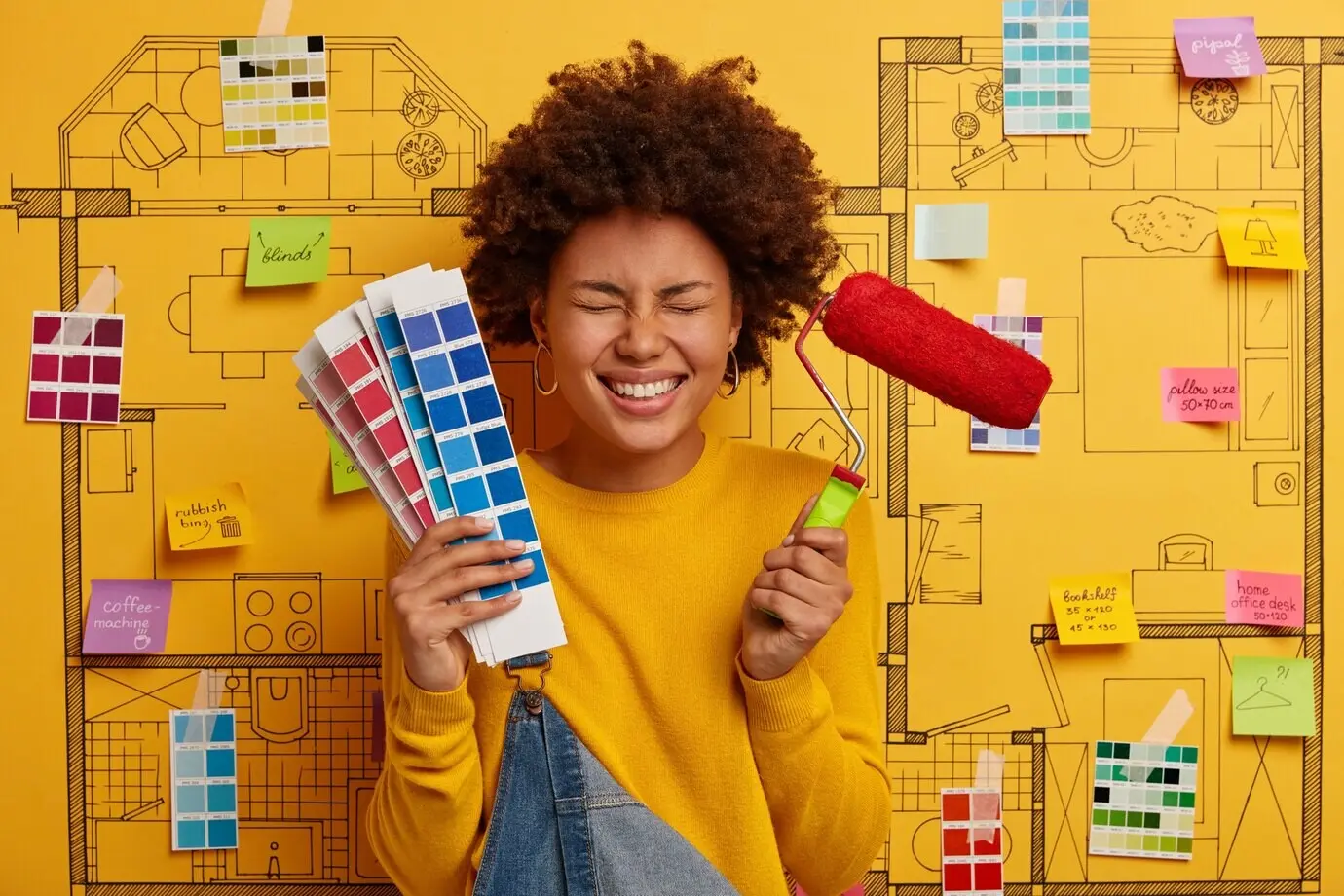 Joyful woman designer holds a paint roller and a color palette, selects the appropriate tone for refurbishment, and is in a good mood.